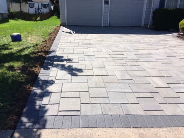 A gray paver driveway with a contrasting stone border leading to a garage