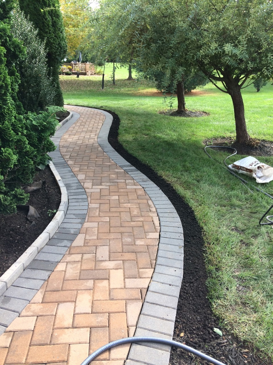 Curving tan and gray paver walk through a landscaped garden