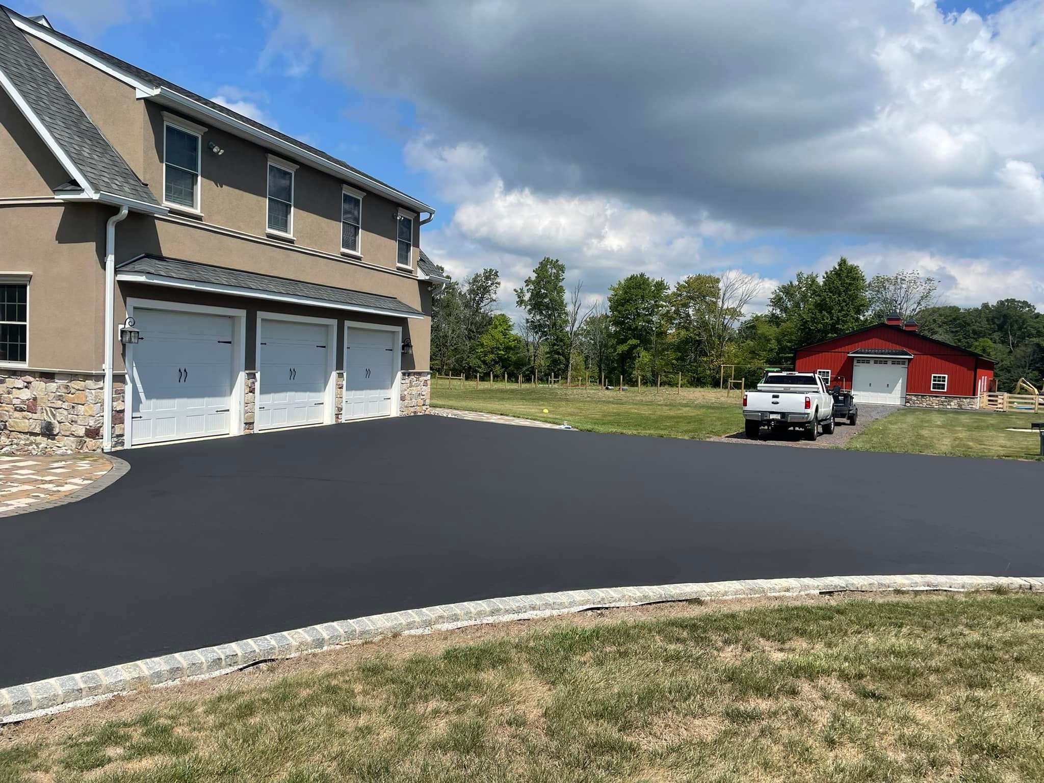 A finished asphalt driveway edged in stone beside a garage