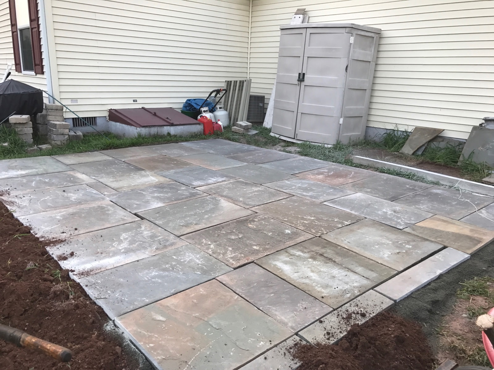 Rectangular stone patio beside a house and garden shed